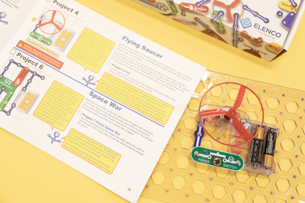 Snap circuits lay against a yellow background next to their instruction book.