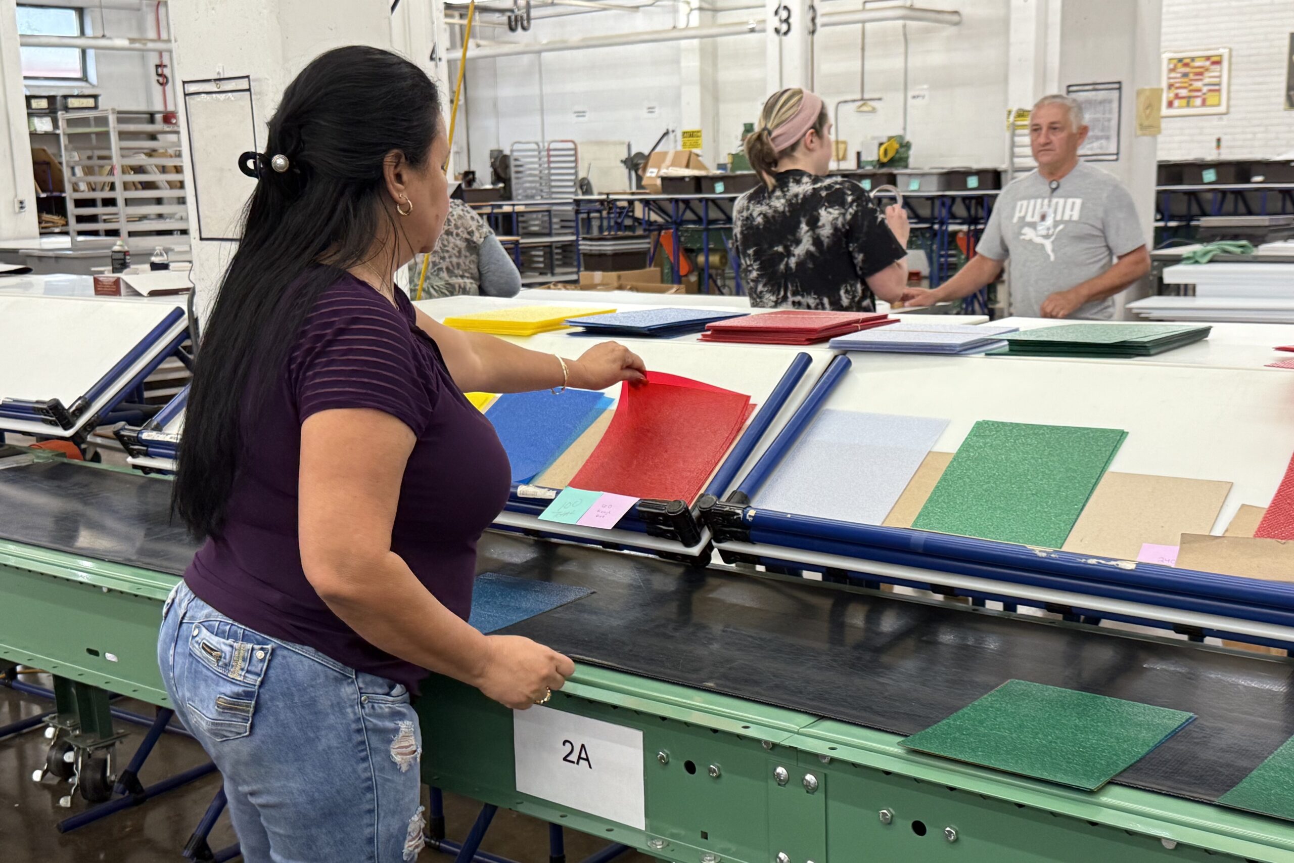 Woman in purple shirt and blue jeans organizing colored sheets of paper in factory assembly line.