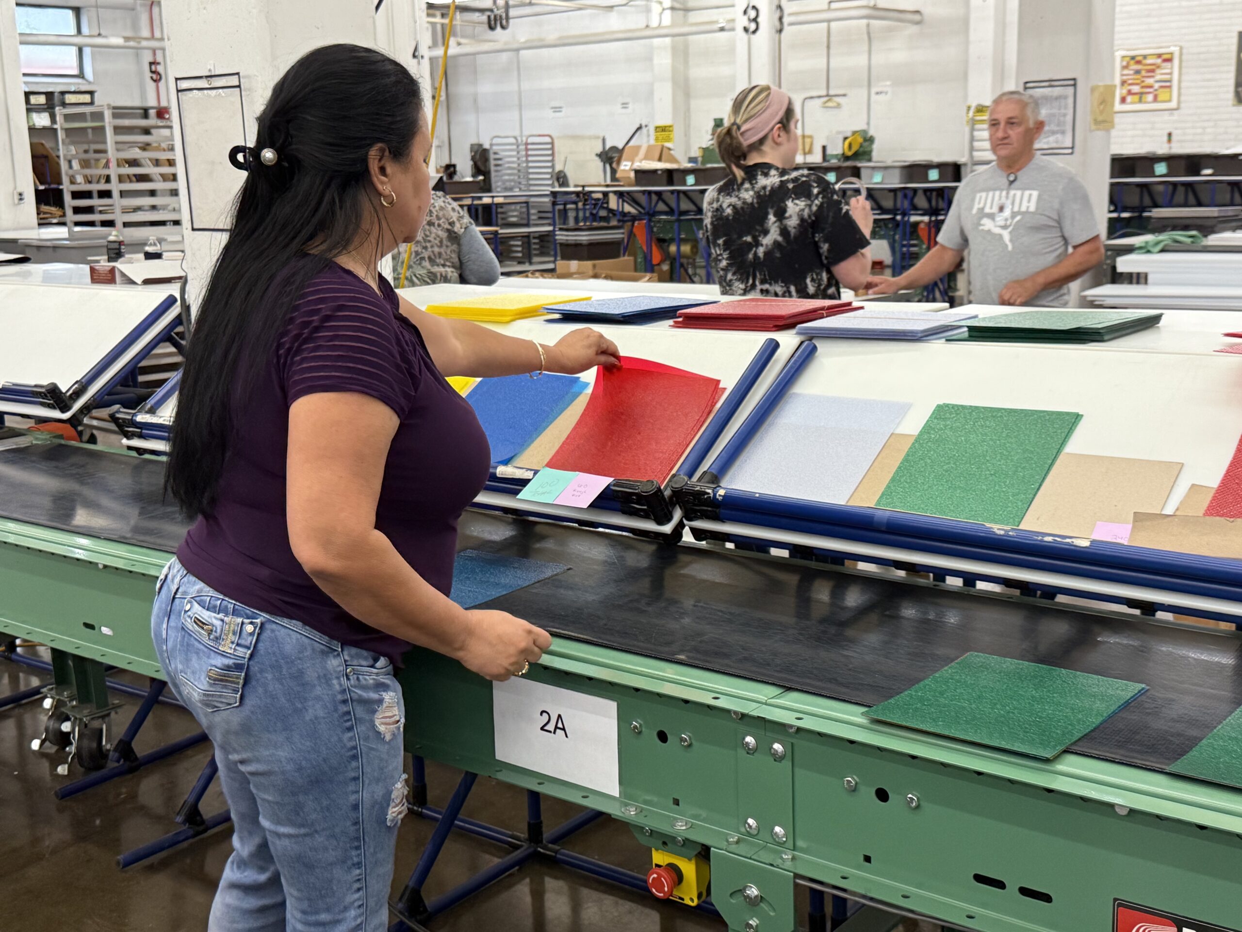 Woman in purple shirt and blue jeans organizing colored sheets of paper in factory assembly line.