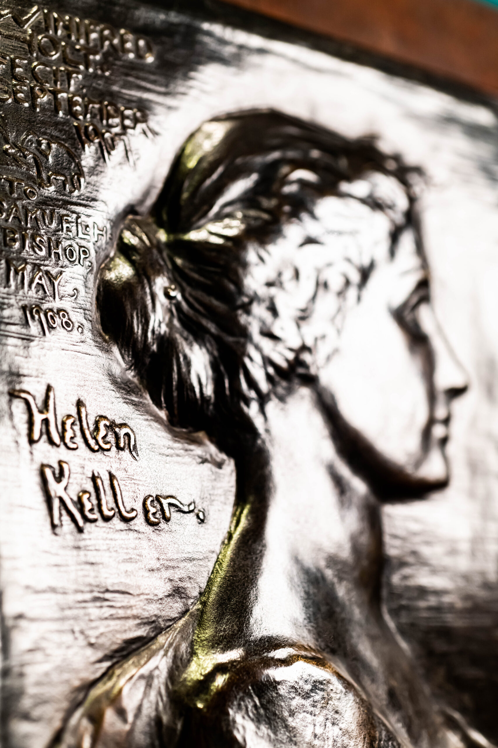 Raised metal portrait of Helen Keller's profile. Text on portrait to the left reads 