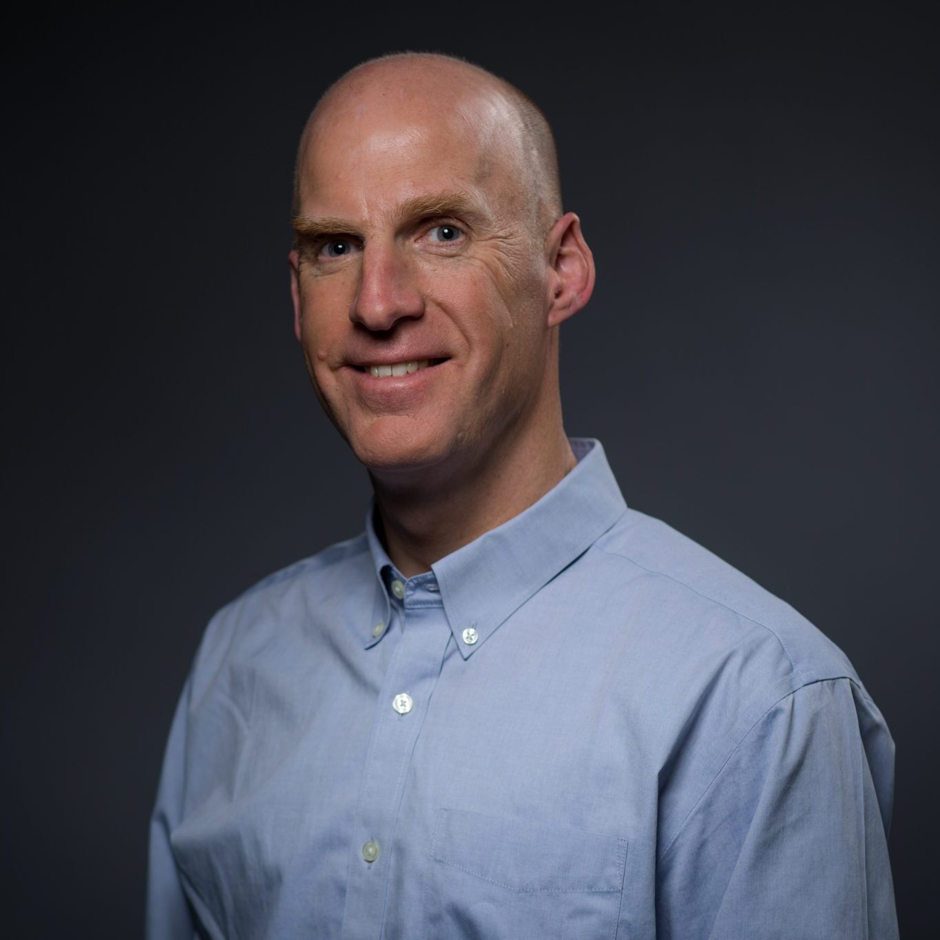 Chris, wearing a blue button down shirt, smiles at the camera.