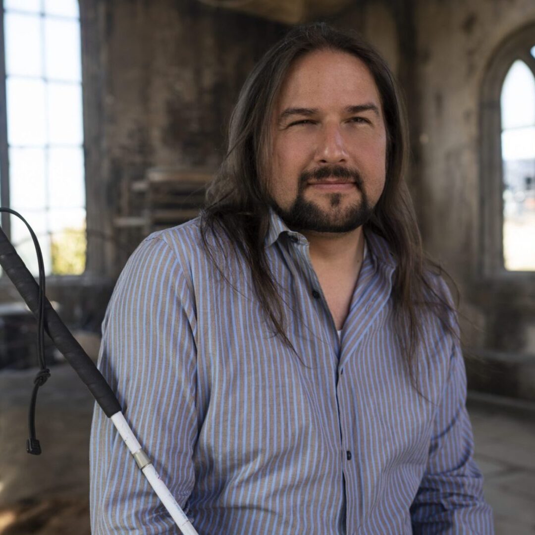 Joe Strechay sits posing for his photo, smiling and holding a cane.