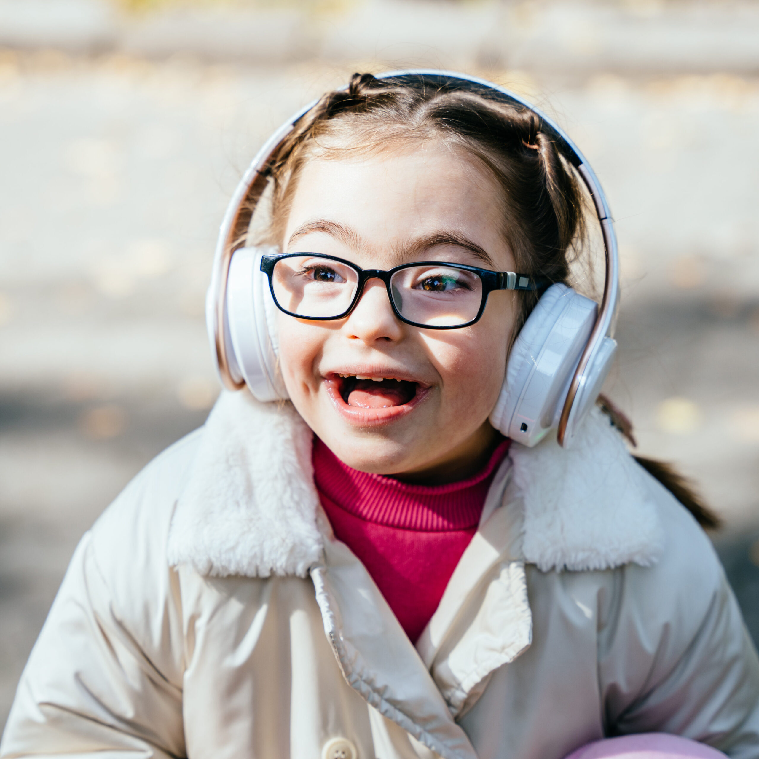A girl wearing headphones and glasses, smiling.