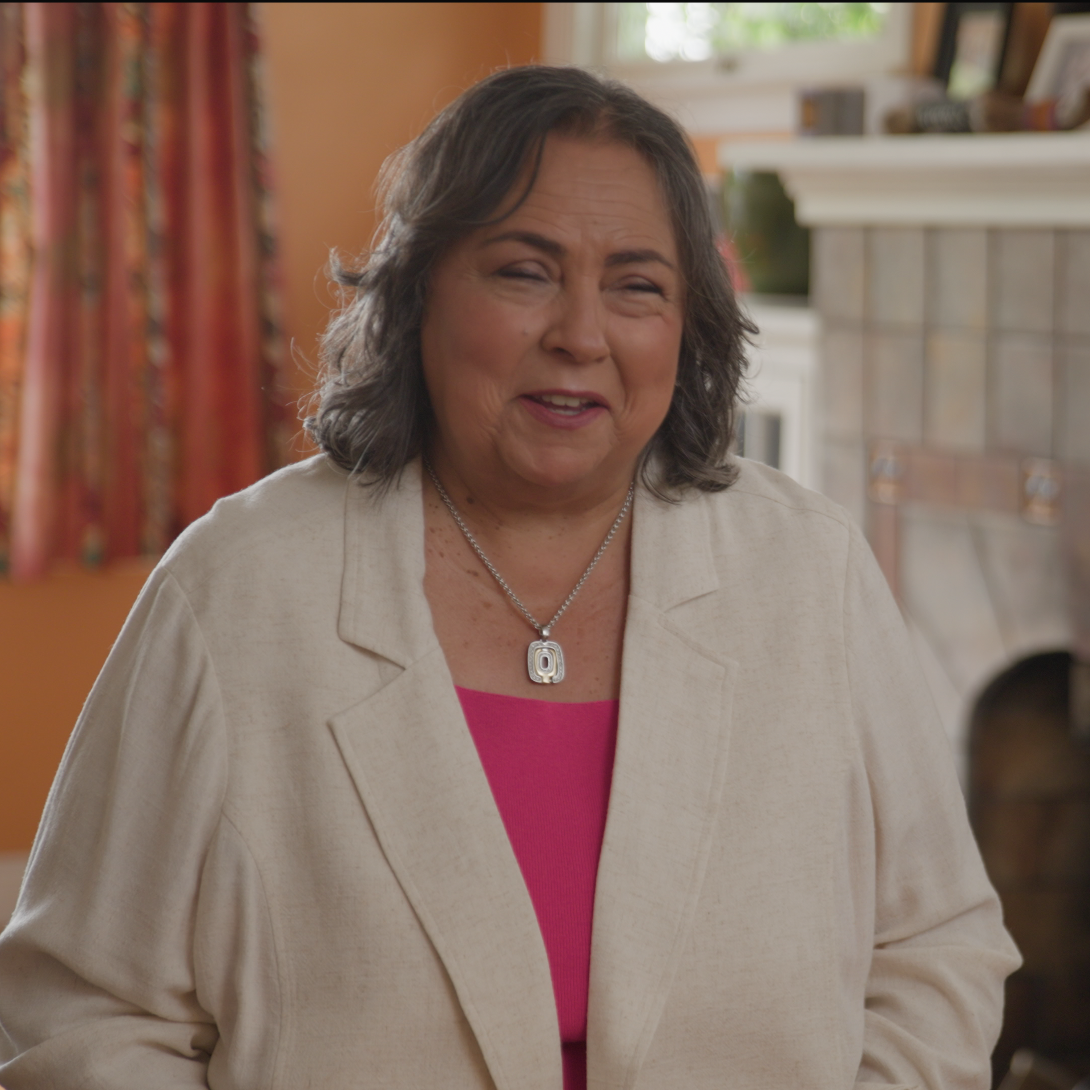 Kathy Martinez smiles back at the camera in a well-lit room with a fireplace and photo frames behind her
