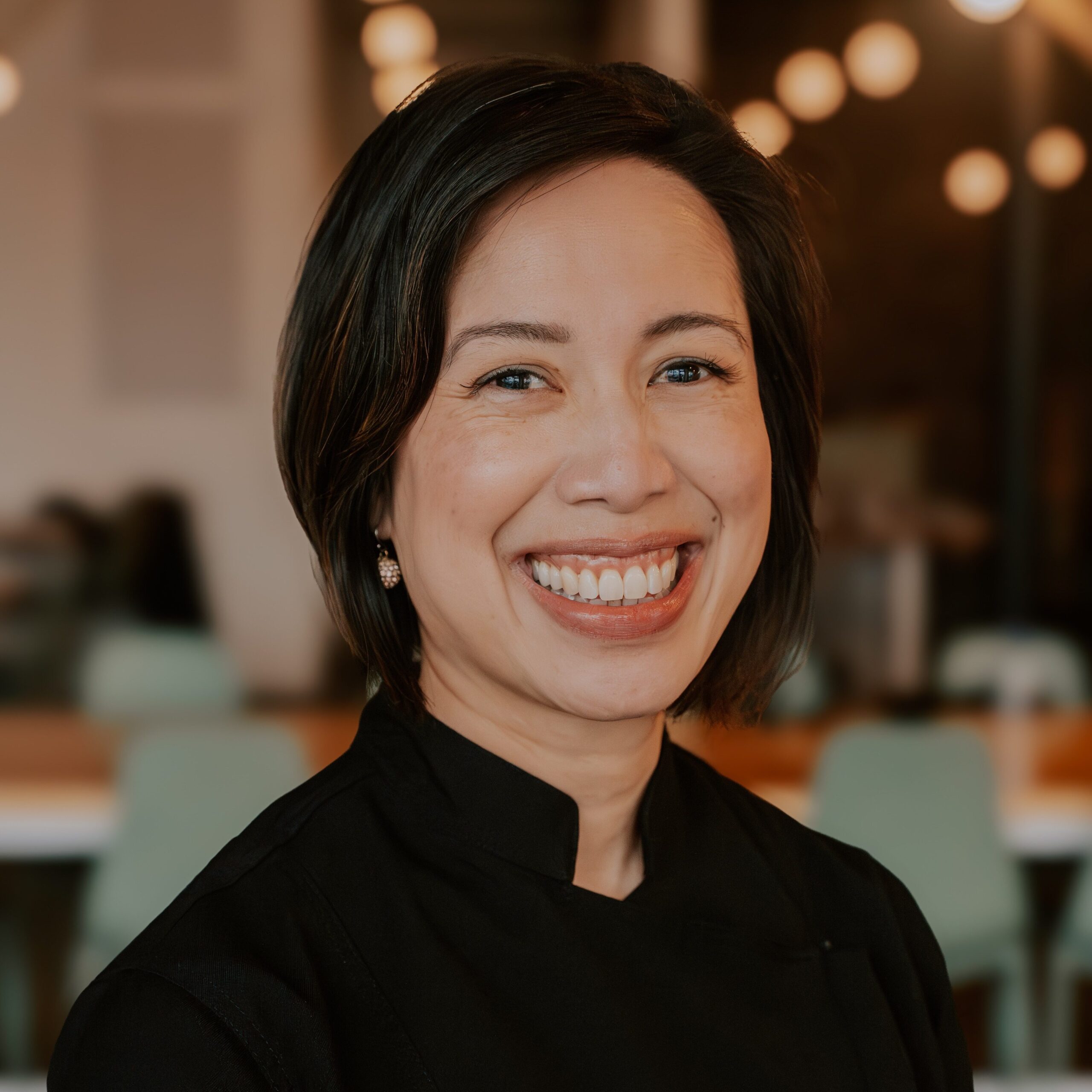 Christine Ha smiles at the camera with a restaurant dining room in the background.