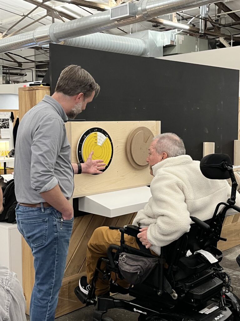 A man in a wheelchair reaches out to touch a tactile model.