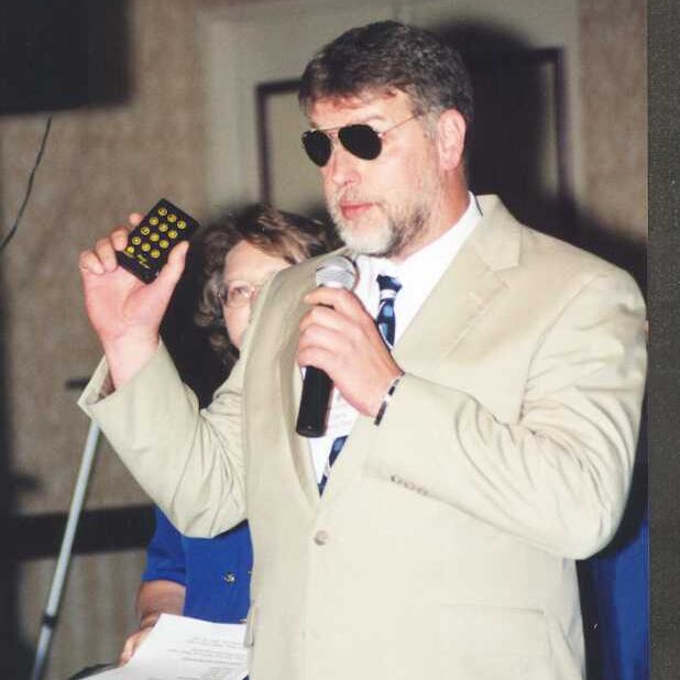 Larry stands with a microphone in his left hand and a piece of tech in his right hand.