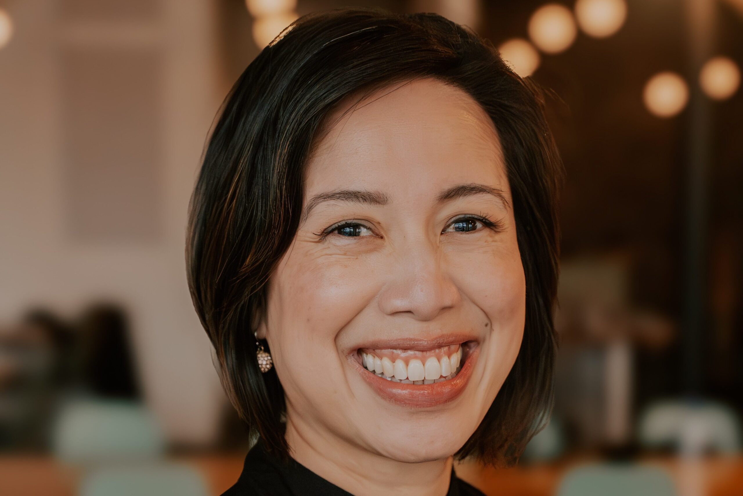 Christine Ha smiles at the camera with a restaurant dining room in the background.