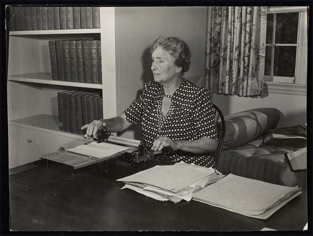 Helen Keller sits behind her desk brailling.