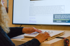 Up close image of hands feeling tactile buttons on a flat surface that are designed to help with navigating on screen media.